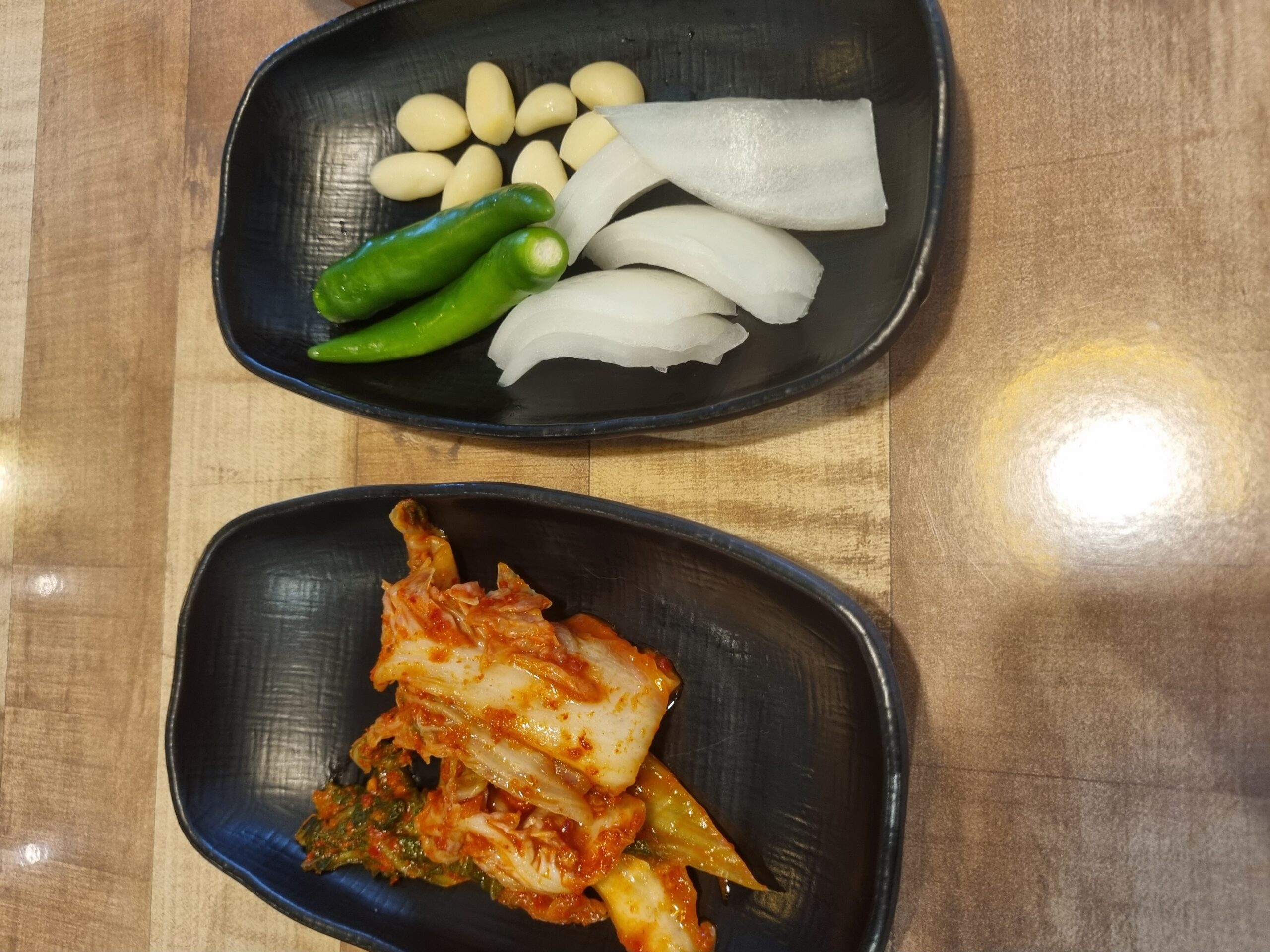 Cabbage kimchi, pickled radish, whole raw garlic cloves and green chillies in a black dish