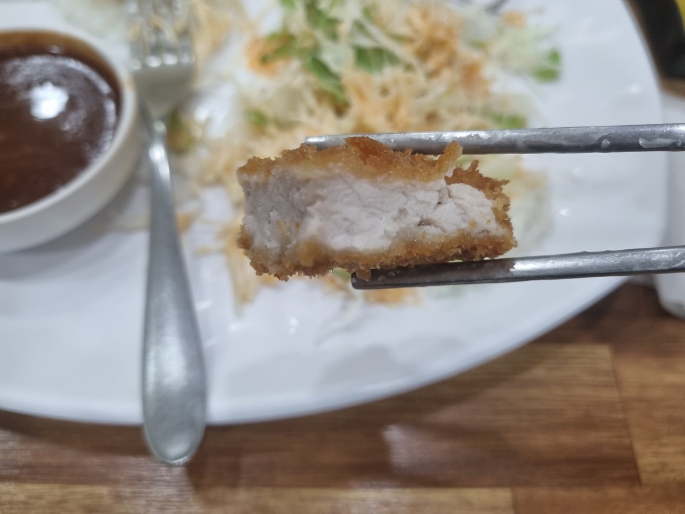 A cross-section of thick fried pork cutlet held in chopsticks