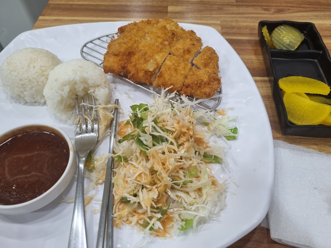 A plate with pork cutlet on a wire rack, rice, cabbage salad, sauce and pickles