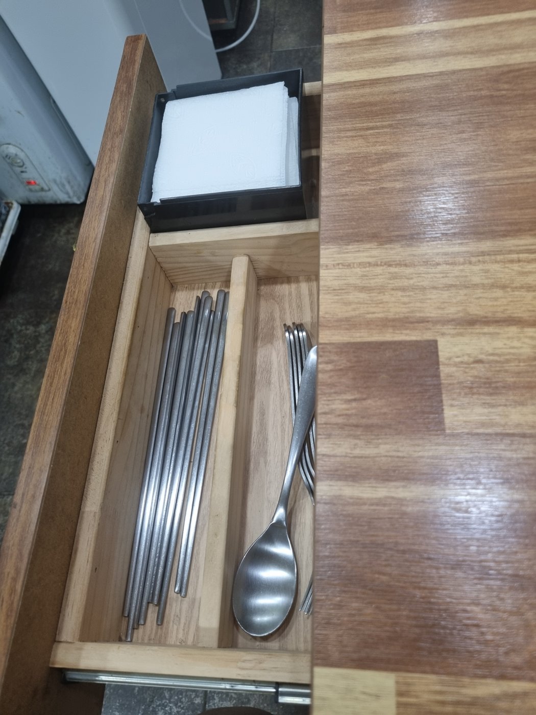 A drawer in the side of a restaurant table holding chopsticks, spoons and napkins