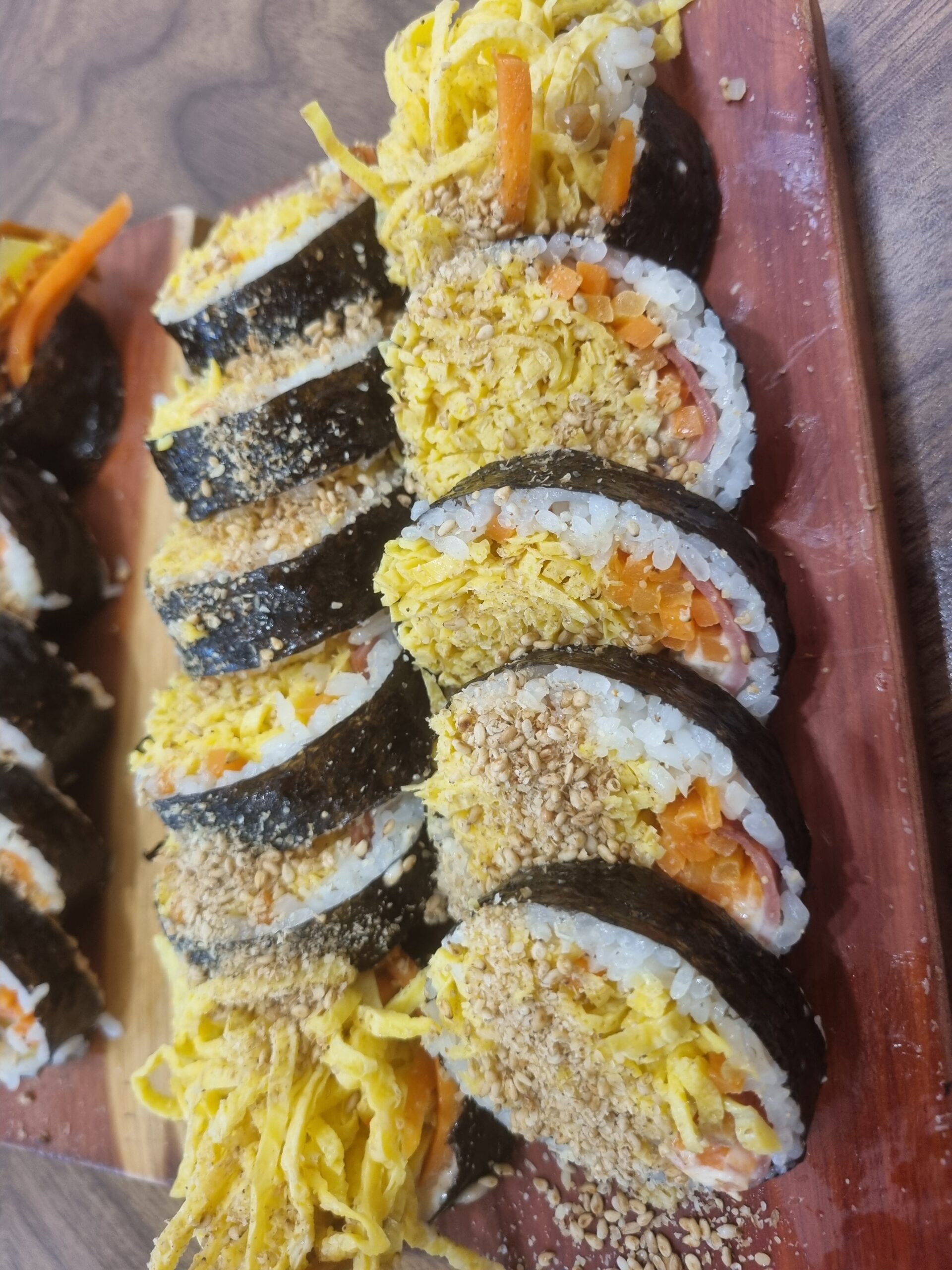 Two rolls of Korean gimbap cut into rounds on a long plate, with egg and pickled radish visible at the open ends