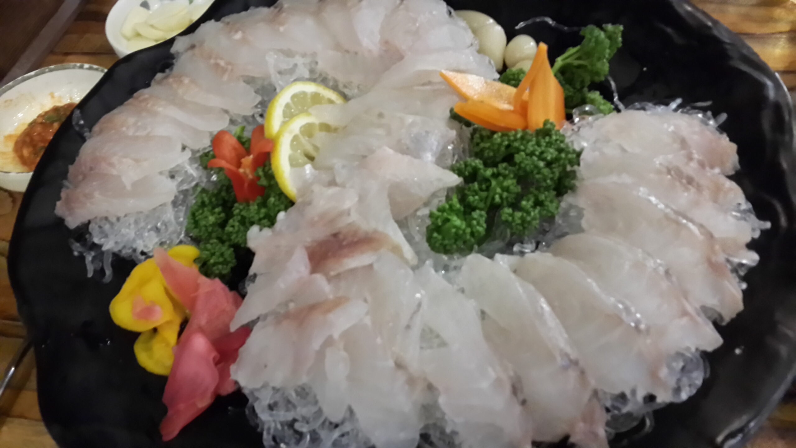 A platter of olive flounder hoe fanned over shaved ice on a black plate, with garnish