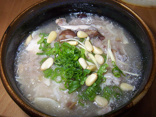 A whole small chicken in clear broth in a stone pot